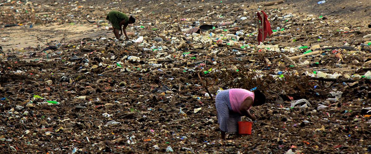 A woman in poverty is looking for something useful on a stinking and smoking, huge landfill.